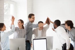 Excited-multiracial-colleagues-celebrating-team-victory-giving-high five-in-office