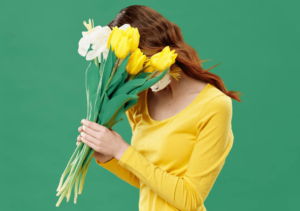 shy-woman-wearing-yellow-dress-hiding-face-behind-flowers