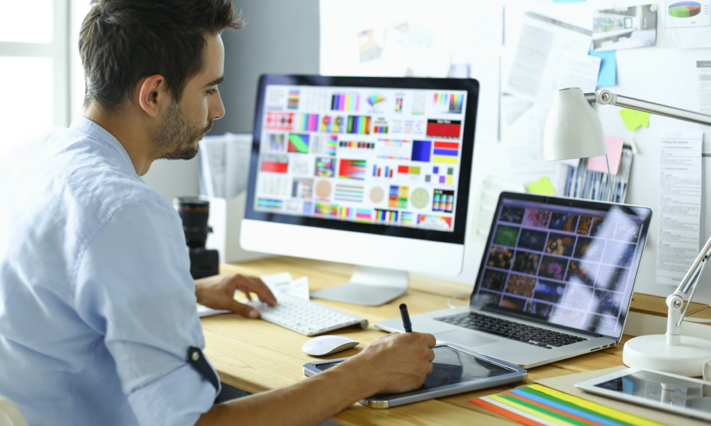 portrait-of-young-designer-sitting-at-graphic-studio-in-front-of-laptop-and-computer-while-working-online