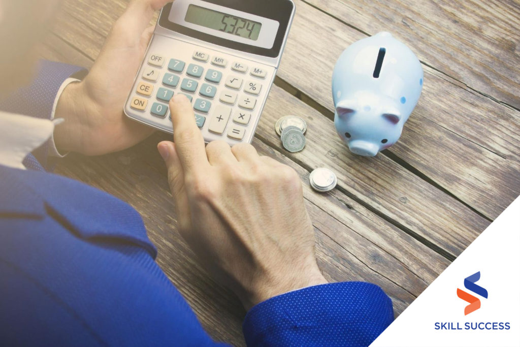 male-financial-analyst-wearing-blue-coat-using-a-calculator-on-a-wooden-table-with-a-piggy-bank-and-coins-on-top