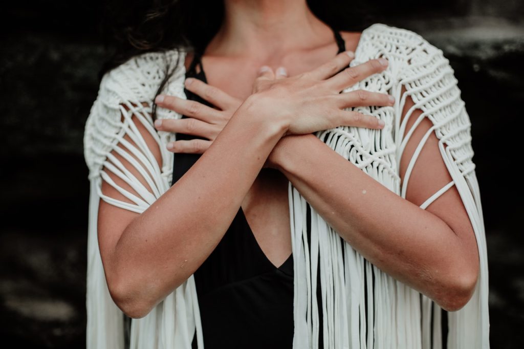 woman wearing white cardigan embracing self