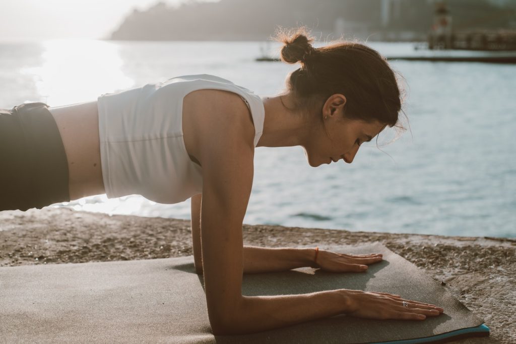 woman in white top doing plank on yoga mat beside the sea