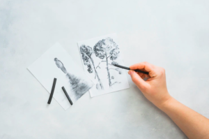 Person's hand sketching beautiful drawing with charcoal stick on white surface Free Photo