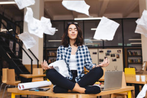 Young pretty joyful brunette woman meditating on table surround work stuff and flying papers