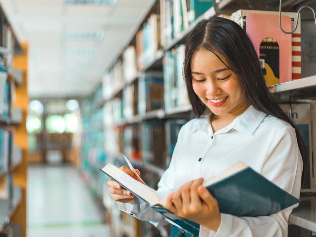 female student reading a book in a library