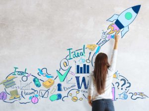 young woman drawing rocket sketch on concrete wall startup concept