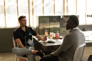 recruiter in black shirt talking to applicant in grey shirt sitting on table