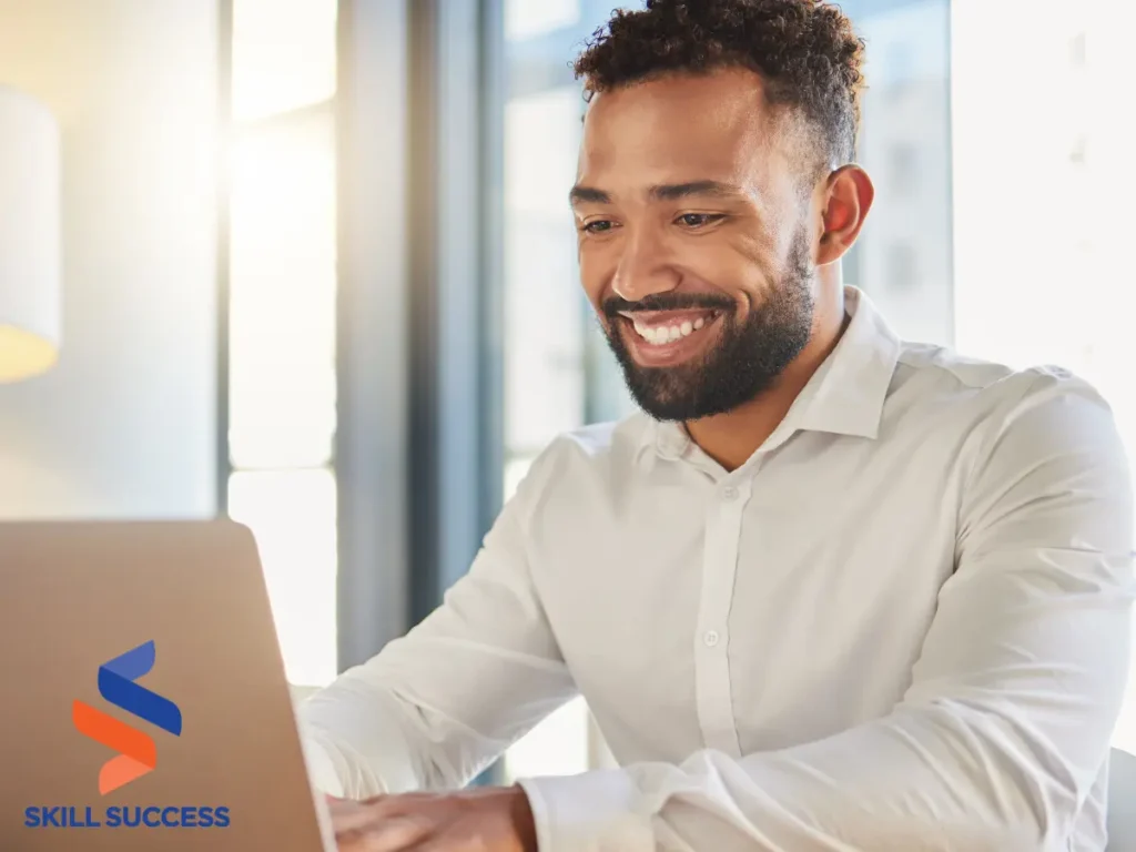 A smiling man sits at a desk, focused on his laptop, creating a positive and productive work environment