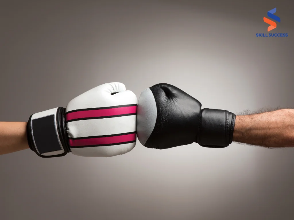 Two individuals holding boxing gloves on a gray background, symbolizing conflict resolution skills in business