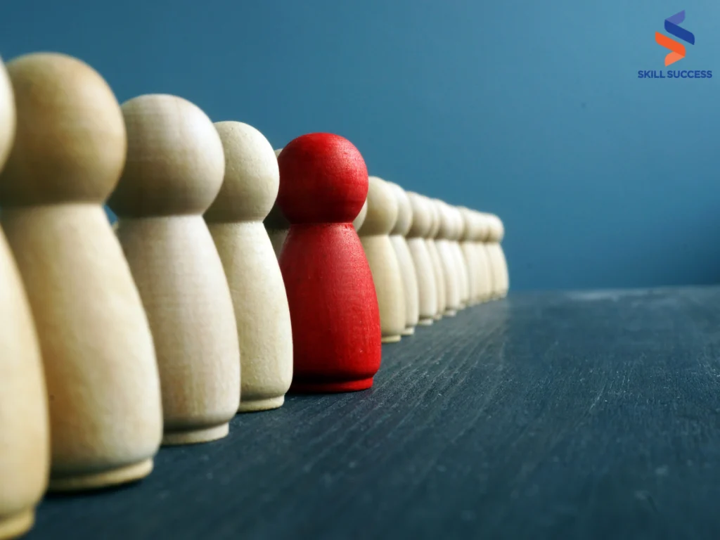 A red figure stands out amidst a group of wooden people symbolizing leadership team development.