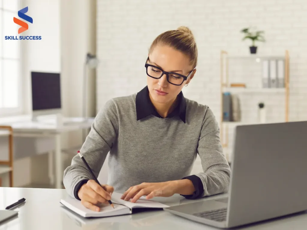 a woman writing notes on a piece of paper beside her laptop while doing a freelance work