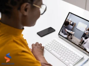 A woman sits at a desk with a laptop, engaging with a whiteboard, illustrating microlearning examples in action