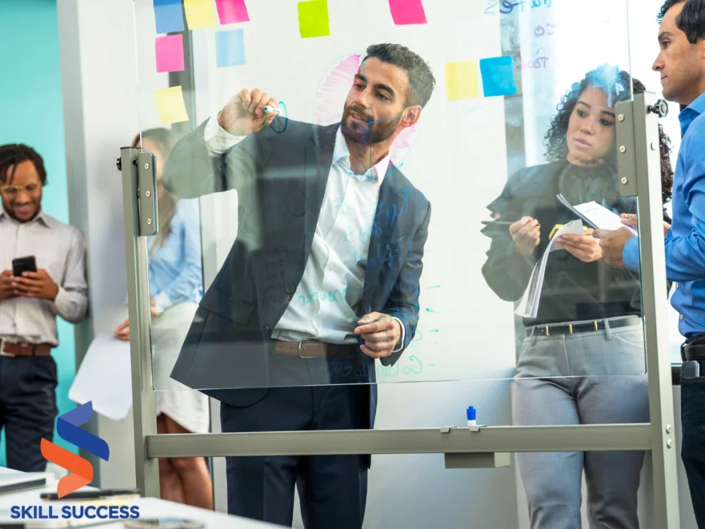 A group of individuals gathers around a glass board, engaging in a leadership training session