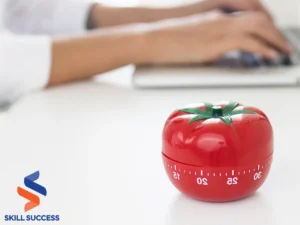 A red tomato with a timer rests on a desk beside a laptop, symbolizing bite-sized training sessions