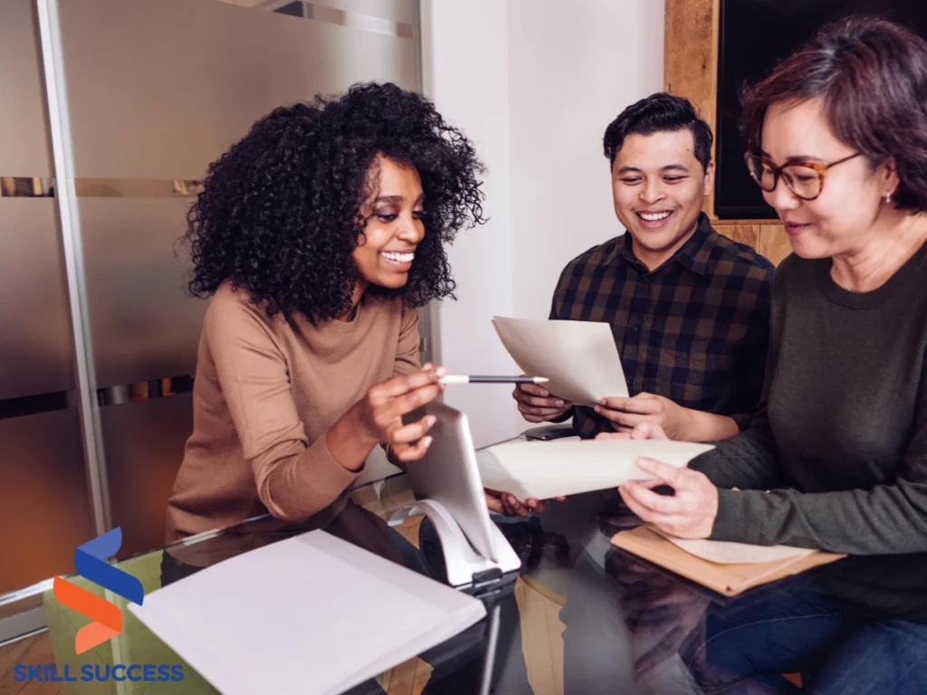 Three individuals engaged in a quick soft skills training session at a table with papers and a laptop.