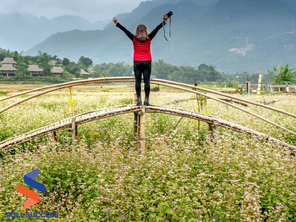 A woman stands on a bridge in a field, arms raised, symbolizing personal growth and empowerment in nature