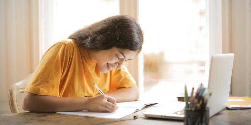 woman in yellow shirt writing on white paper