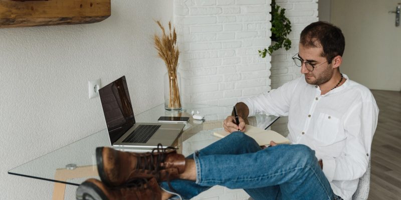 man in white dress shirt and blue denim jeans sitting on wooden chair and writing his long term career plan