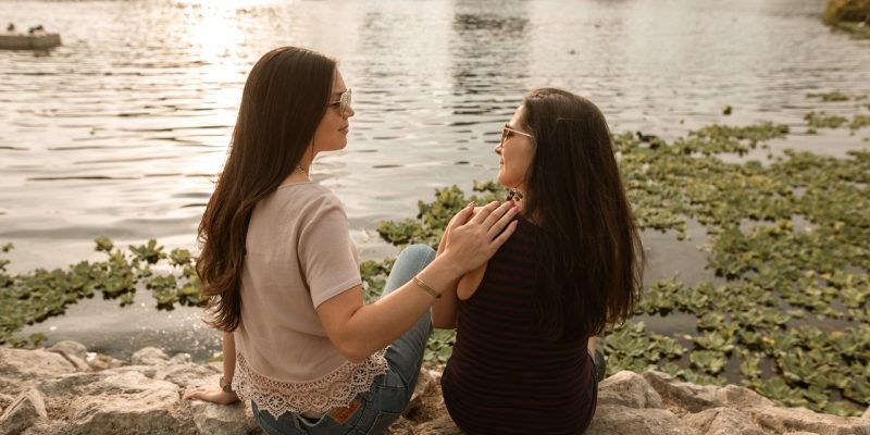 two women sitting by a lake