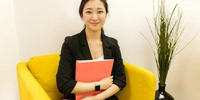 female job applicant in black blazer sitting on yellow armchair