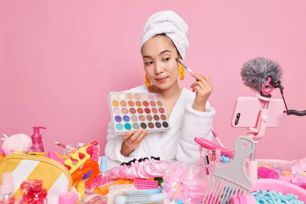 Professional woman beauty blogger streams video about makeup applies colorful shadow with cosmetic brush holds palette records online beauty course