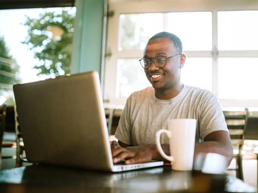 man in cafe wearing grey shirt typing on laptop