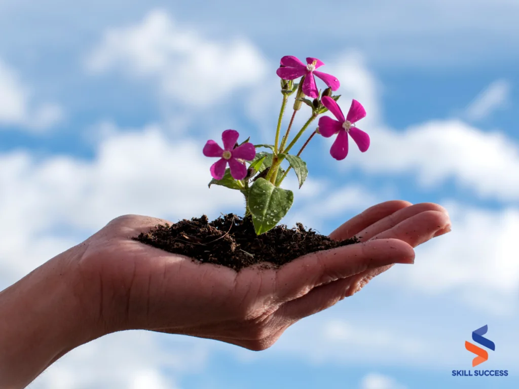 A hand nurturing a small plant with purple flowers, symbolizing self-development and growth