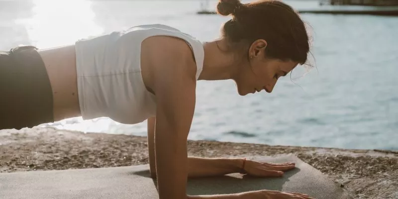 woman in white top doing plank on yoga mat beside the sea